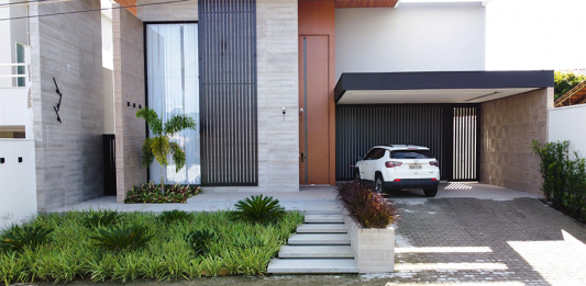 Refúgio Tropical: Paisagismo Minimalista Valoriza Residência em Sapucaia-RJ Paisagismo residencial por Studio Julio Sousa Paisagista| Fachada da casa com canteiro de pinheiros-de-buda