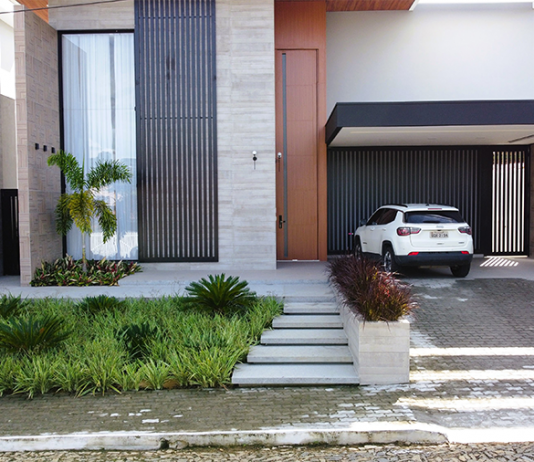 Refúgio Tropical: Paisagismo Minimalista Valoriza Residência em Sapucaia-RJ Paisagismo residencial por Studio Julio Sousa Paisagista| Fachada da casa com canteiro de pinheiros-de-buda