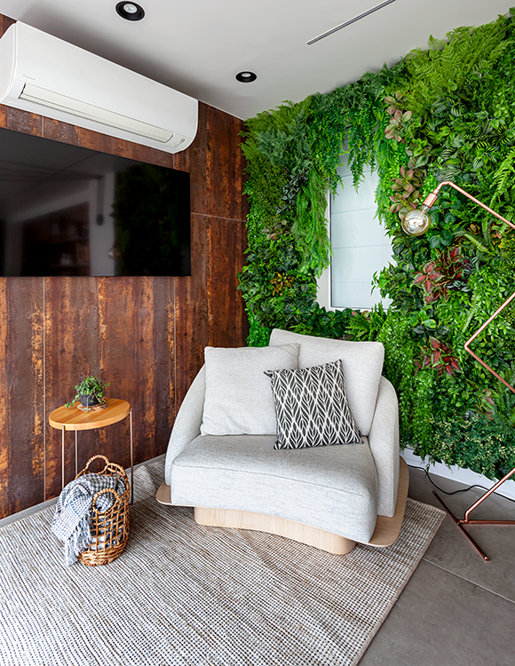 Na face oposta da varanda, a arquiteta Cristiane Schiavoni propôs um cantinho de leitura com luminária que imprime sofisticação, poltrona aconchegante e mesinha de apoio. O jardim vertical completa a decoração, emoldurando o espaço