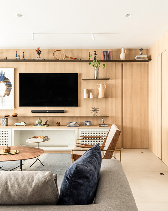 Na sala de estar desse apartamento, o arquiteto Bruno Moraes lançou mão da porta mimetizada para ocultar o acesso ao corredor que dá acesso à ala íntima