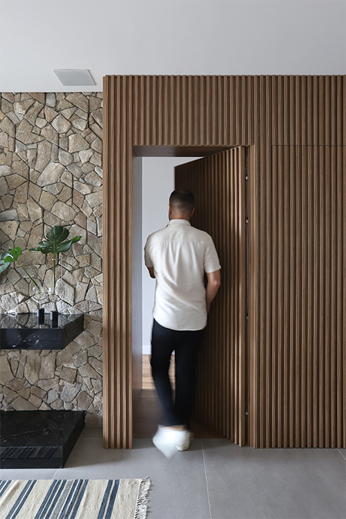 Camuflada no painel ripado, a portas mimetizadas concebidas pelo arquiteto Bruno Moraes resguardam a entrada do lavabo e do dormitório