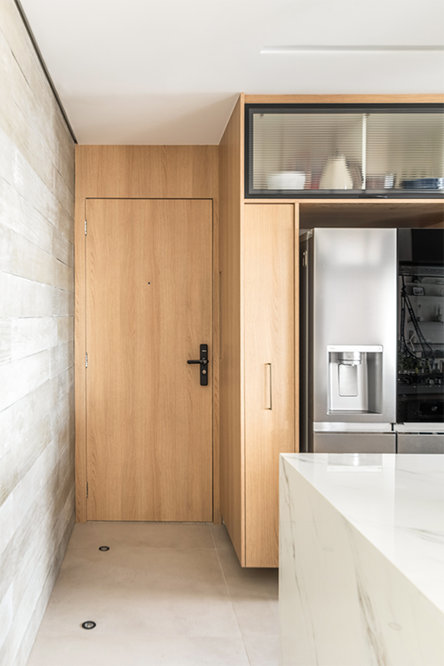Nesse apartamento, o arquiteto ocultou a porta do hall de serviço na cozinha, de forma com que se integrasse à marcenaria planejada. O projeto também ganhou em absorção acústica, uma vez que se concebeu uma camada extra de isolamento de som