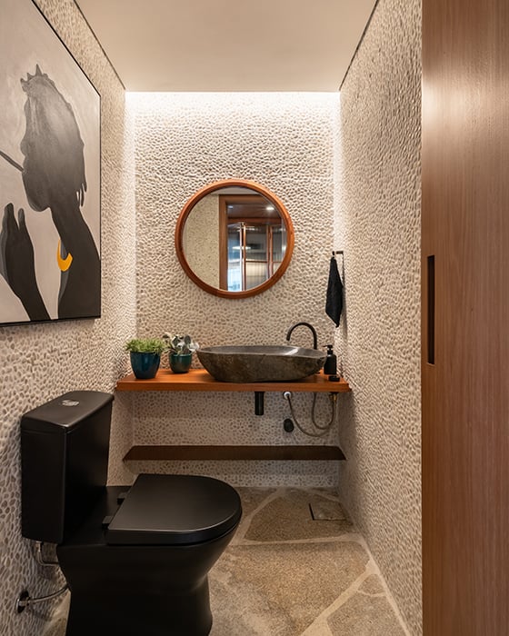 Projeto: Labra Arquitetos| No Lavabo, as profissionais optaram por uma cuba em pedra natural em harmonia com a bancada de madeira de demolição, bacia em preto e seixos brancos na parede