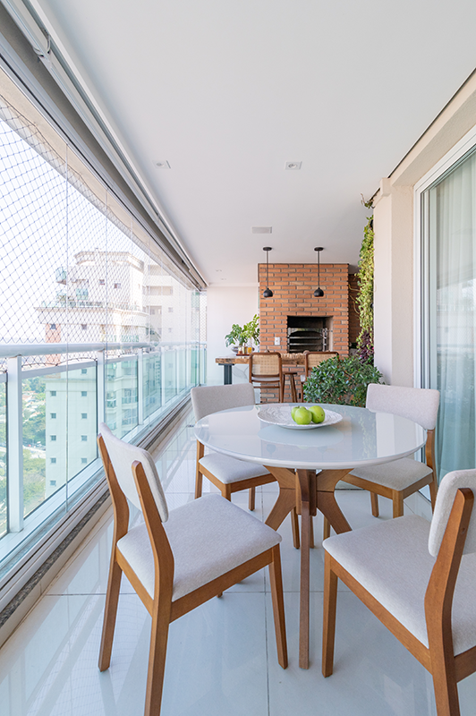 A varanda gourmet conta com churrasqueira, parede verde, aparador e mesa com cadeiras, tudo isso com uma bela vista da cidade | Projeto: Isabella Nalon