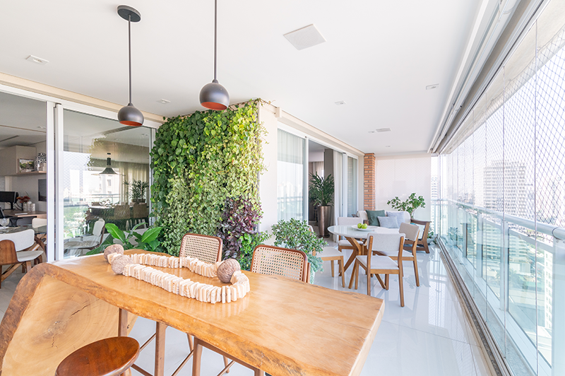 A varanda gourmet conta com churrasqueira, parede verde, aparador e mesa com cadeiras, tudo isso com uma bela vista da cidade | Projeto: Isabella Nalon