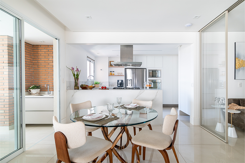 Os moradores podem escolher se deixam as portas de vidro abertas ou fechadas de acordo com o período do dia e a necessidade do momento. Do lado esquerdo há uma integração com a varanda gourmet e, do lado direito, outra sala que abriga uma mesa de trabalho para duas pessoas | Projeto de Isabella Nalon