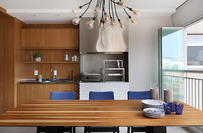 Projeto: RMV Interiores | Pendentes, cores vibrantes e móveis integrados criam um ambiente elegante e funcional, com destaque para a área gourmet, boiseries e plantas que completam a composição.