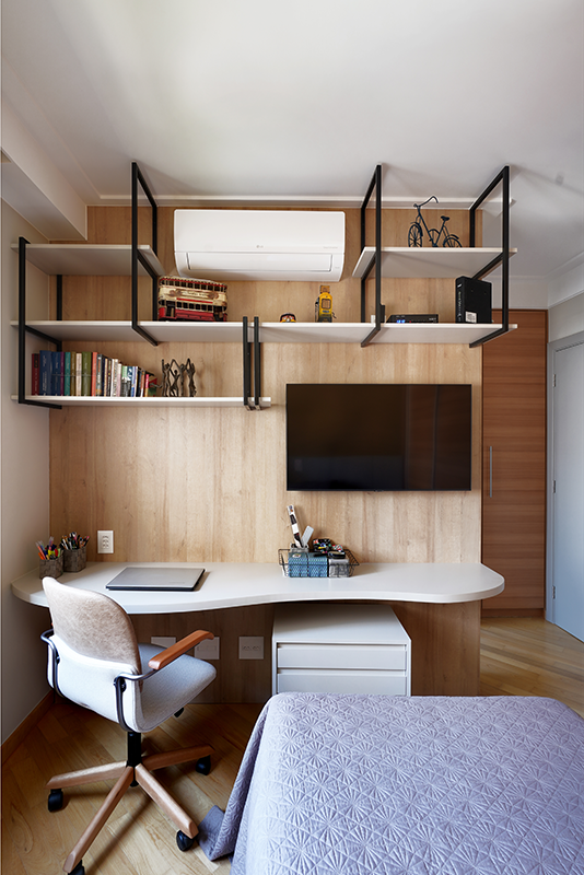 No home office com a mesa em formato orgânico, o painel de madeira com as prateleiras suportadas pela serralheria preta ajuda a manter os itens sempre organizados. Por lá, a cama está sempre pronta para receber os hóspedes com total comodidade | Projeto: Rosangela Pena Arquitetura
