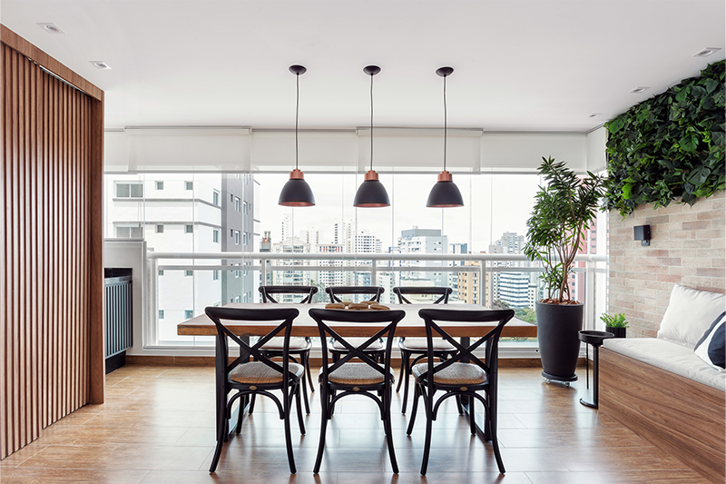 Projeto: RMV Interiores | Varanda gourmet com detalhes em preto, tijolos e jardim vertical, tendo a mesa de madeira de demolição como protagonista para encontros e celebrações.