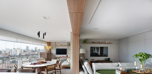 Reforma de apartamento explora dimensões generosas da varanda e agrega soluções como a inserção de um passa-prato na cozinha Projeto: Rosangela Pena Arquitetura | Entre a sala de estar e a varanda, a arquiteta Rosangela Pena valorizou a viga existente ao revesti-la com madeira. A 'divisão' sutil entre os ambientes tornou-se ainda mais elegante.