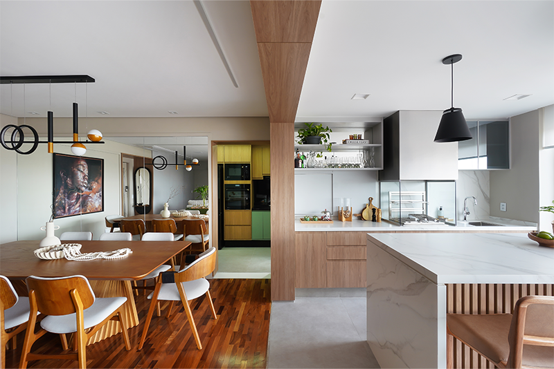 Projeto: Rosangela Pena Arquitetura | Como um pórtico, a viga revestida em madeira harmoniza com os tons da marcenaria da área gourmet e do ripado da bancada. Já na sala de jantar, o espelho amplia visualmente o ambiente.