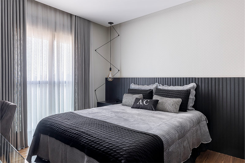 Projeto: Spaço Interior Arquitetura | No dormitório o cinza domina em elementos como parede, cabeceira e enxoval. No banheiro da suíte, o revestimento claro com efeito de pedra destaca os detalhes pretos e a marcenaria da bancada.