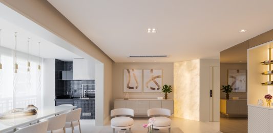 Aconchego sem madeira em apartamento sofisticado criado por Sabrina Salles Projeto: Sabrina Salles | Sala de jantar ganha sofisticação com buffet em pedra translúcida iluminada lateralmente e cristaleira bar em vidro reflecta.
