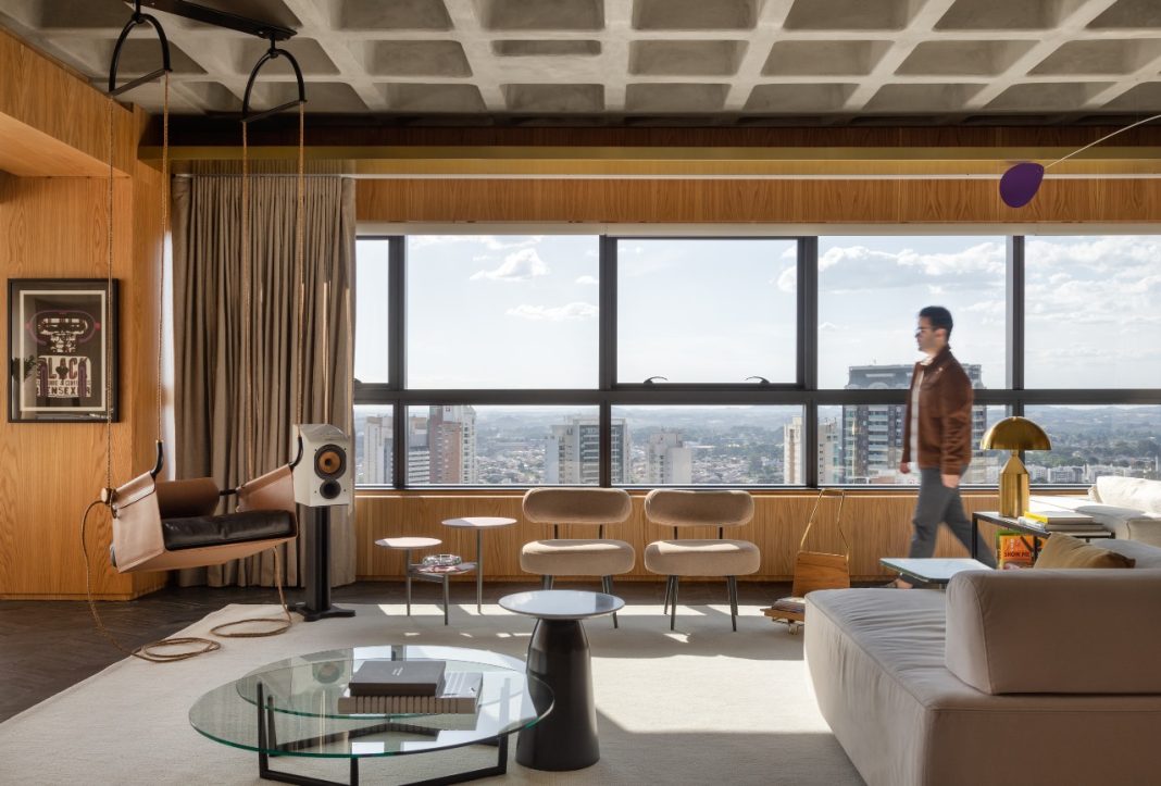 Rodolfo Fontana v1 Projeto: Rodolfo Fontana | A área social do Apartamento Mike combina a imponência da laje aparente com mobiliário contemporâneo e vistas panorâmicas da cidade, em um espaço que equilibra linguagem industrial e conforto.