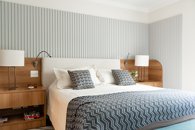 Projeto: Juliana Fabrizzi | Tons suaves e texturas acolhedoras compõem um refúgio sereno, com painel ripado azul e cabeceira estofada.