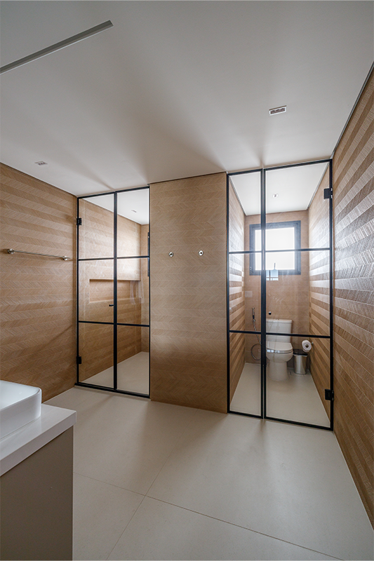 Projeto: Yannick Athia | Banheiros que se complementam: o principal, com duas cubas e cabines separadas; e o segundo, em tons de verde suave, traz leveza e continuidade ao projeto