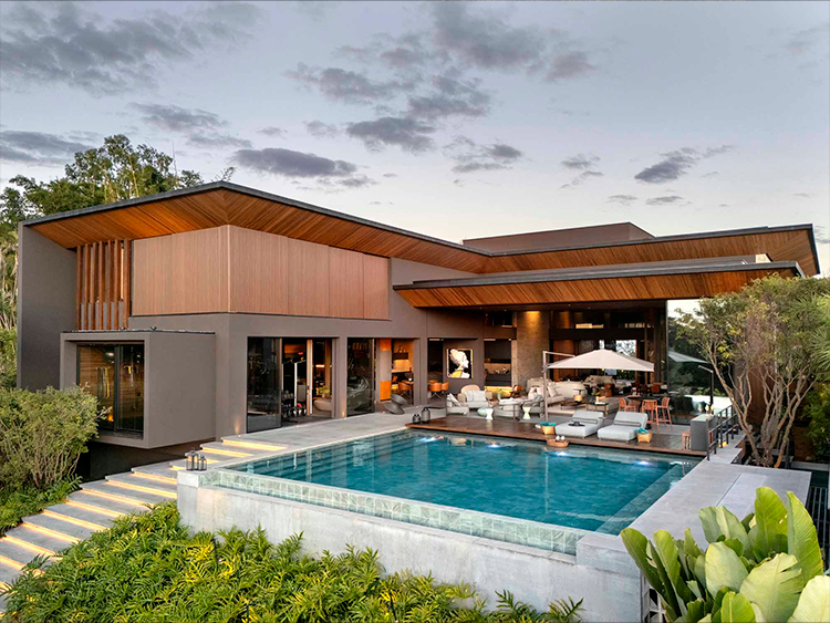 Neste projeto, a vegetação foi cultivada de forma estratégica e em nível inferior ao da piscina para valorizar a vista panorâmico. Ao fundo, ao lado direito do deck, é possível observar uma árvore Pau Brasil com a função de trazer mais privacidade ao vizinho.