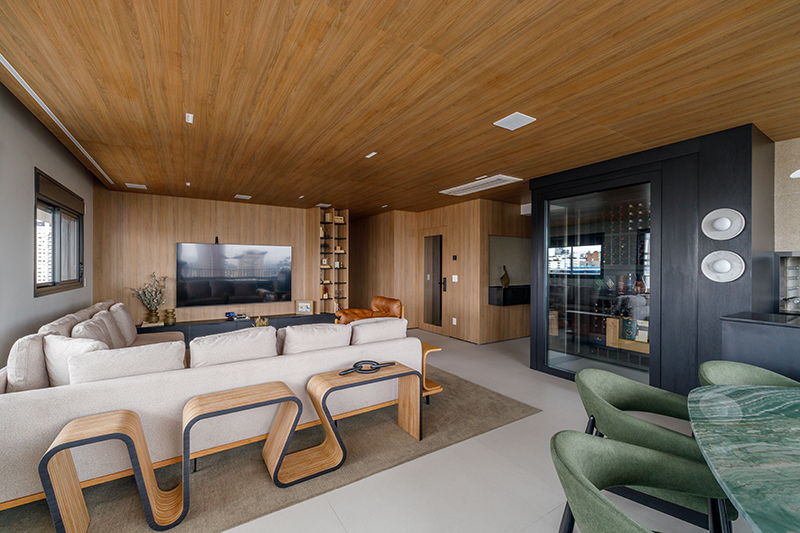 Projeto: Yannick Athia | Sala de jantar conectada à área social, destacando móveis com tampos orgânicos e a atmosfera acolhedora criada pela marcenaria em madeira.