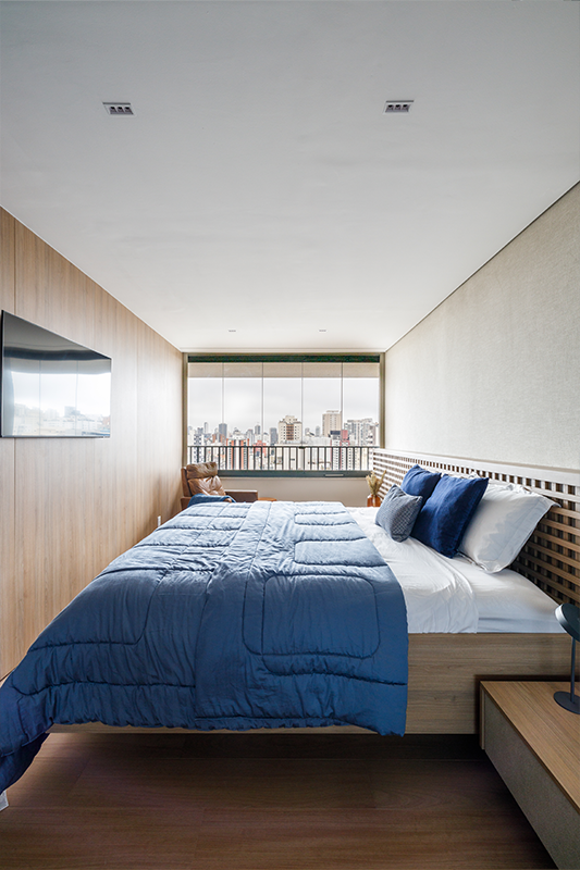 Projeto: Yannick Athia | Suíte ampla e acolhedora, com integração à sacada e cabeceira em muxarabi retroiluminado; cama sob medida, armários com portas de vidro e papel de parede em linho acrescentam textura e serenidade ao ambiente.