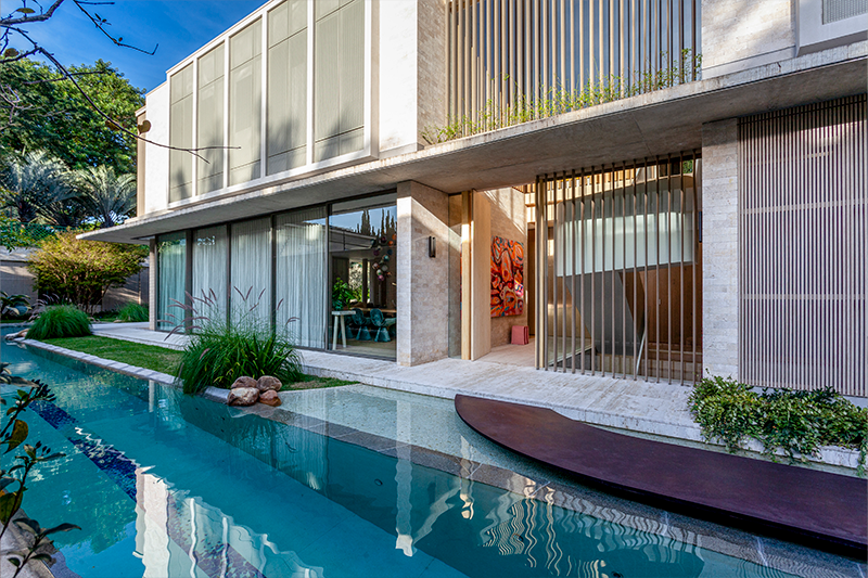 Projeto: BZP Arquitetura | A passarela de acesso em aço, apoiada sobre pedras de granito rústico, se destaca como uma escultura funcional e conduz à área da piscina, reforçando a integração entre arquitetura, jardins e lazer na residência assinada pela BZP Arquitetura.