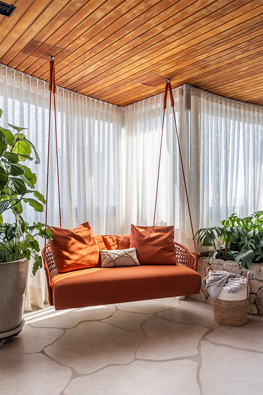 Projeto: Cilene Lupi | O teto revestido com madeira combinado com sofá suspenso laranja são pontos de cor e elementos que transmitem conforto para varanda