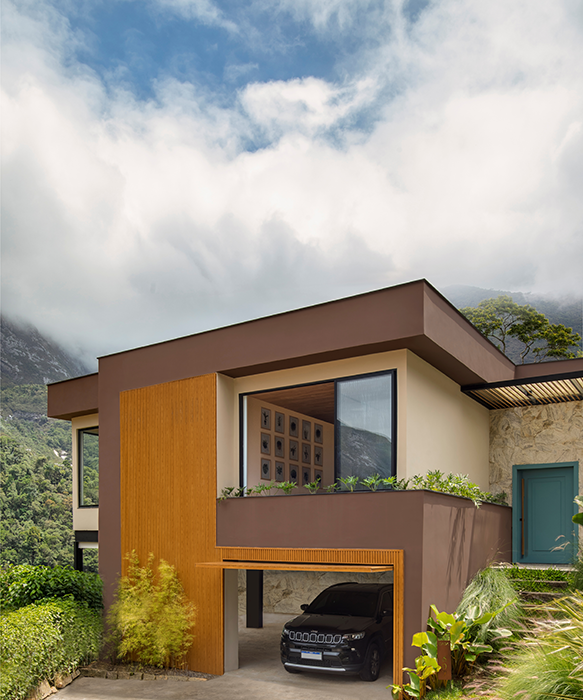 Projeto: Felipe Rohen Arquitetura | Antes e depois da fachada: a antiga construção colonial de tijolinhos deu lugar a uma nova linguagem contemporânea, marcada por linhas retas, pedras naturais e portas em azul vibrante.