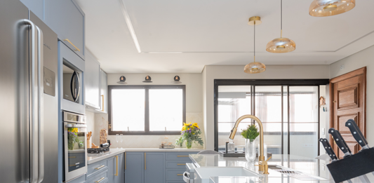 Juntas, porém delimitadas: a importância da oferecer a independência entre a cozinha e a área de serviço nos projetos residenciais Projeto Mari Milani| Cozinha ampla com ilha central e marcenaria em azul claro. A área de serviço fica integrada, mas discreta, graças à porta de serralheria com vidro canelado, garantindo luz natural e organização.