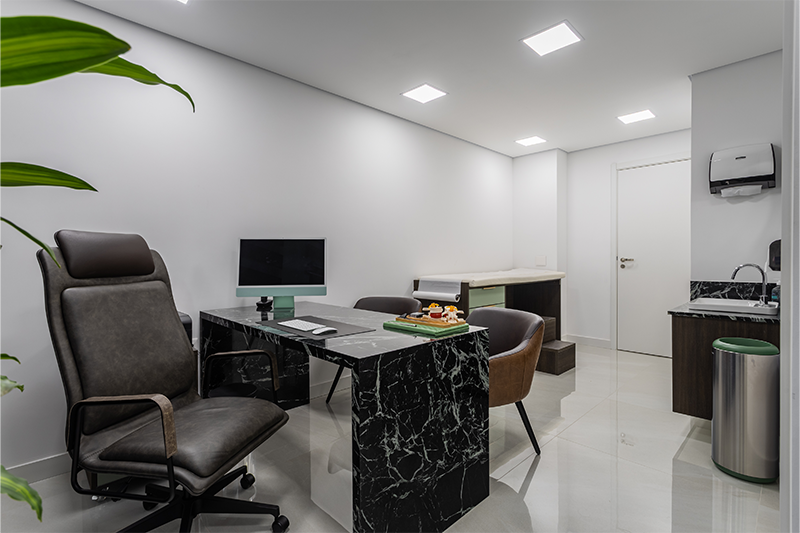 Projeto: Camila Palladino | Mármore Verde Alpi, marcenaria em tons mais profundos e poltronas confortáveis criam uma sala de atendimento intimista e acolhedora