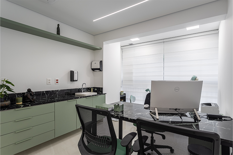 Projeto: Camila Palladino | Na segunda sala, o verde da marcenaria se harmoniza ao Mármore Verde Alpi, enquanto a mesa com estrutura metálica adiciona um toque contemporâneo à composição