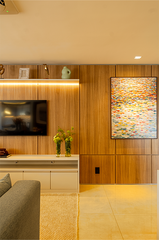 A marcenaria ganha protagonismo com o painel de madeira que aquece o ambiente, enquanto os espelhos ampliam a luz e trazem leveza ao espaço. O resultado é um equilíbrio elegante entre conforto, estética e funcionalidade