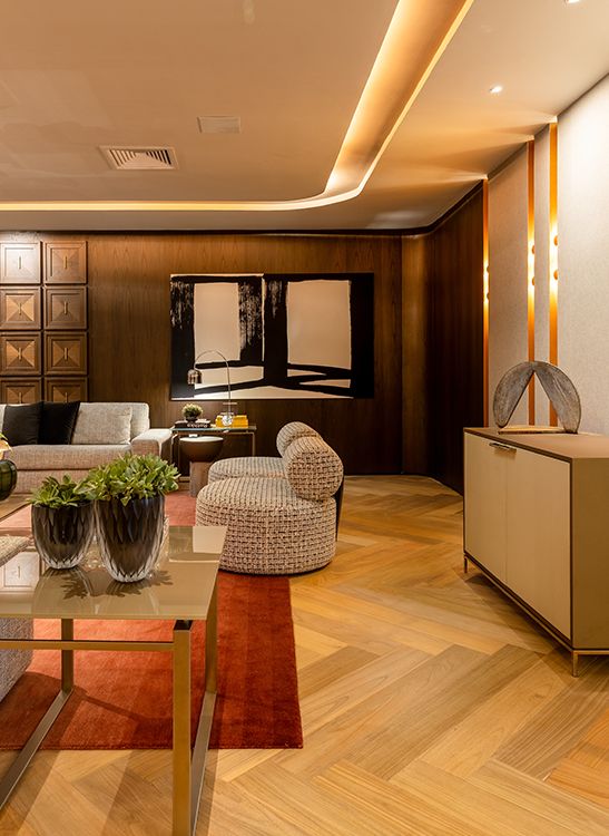 Com revestimentos nos tons de madeira – mais claro para o piso e mais escuro para o painel da parede –, a arquiteta Patricia Penna elegeu a intersecção entre o cinza e o preto, além do terroso representado pelo tapete.