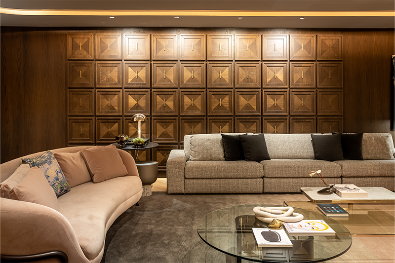 No living, as boiseries de madeira com marchetaria rememoram o adorno clássico das paredes sob um olhar atual, criando um verdadeiro painel que inspira elegância ao ambiente